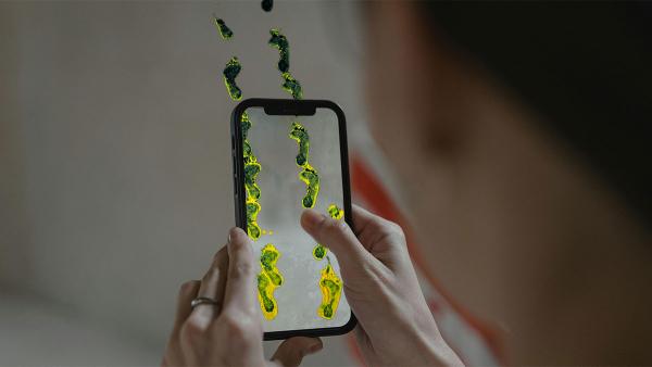 A woman using her phone to watch an augmented reality film. The screen shows footsteps walking across a room